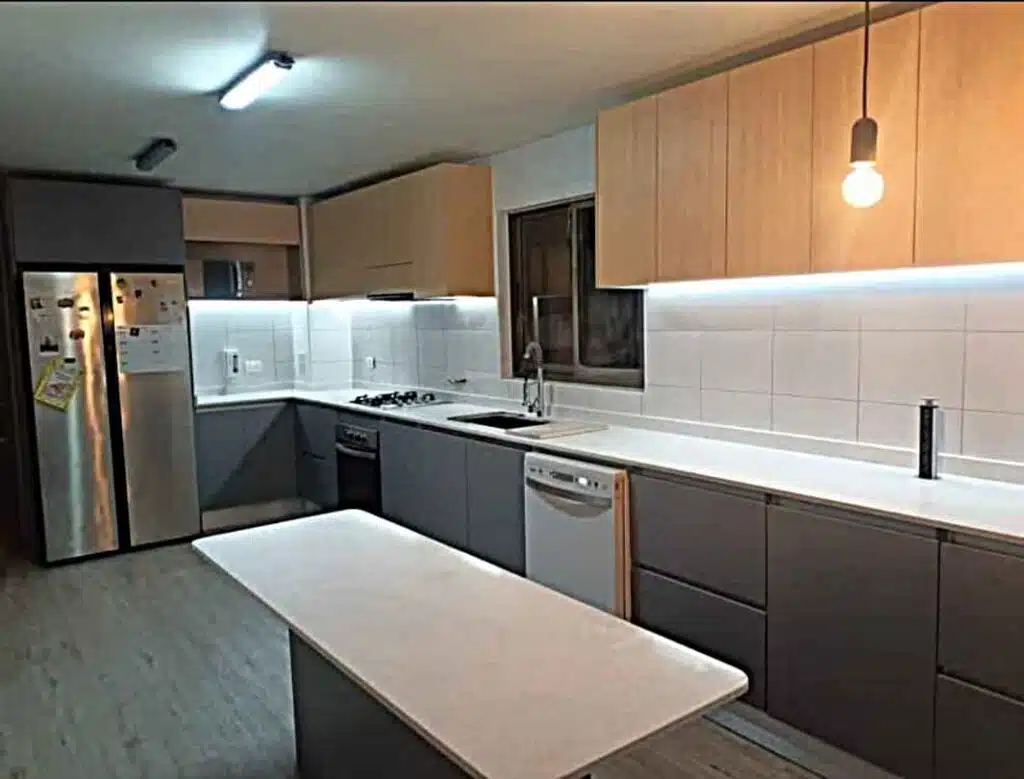 Cocina a medida en Santiago con muebles en tonos madera y gris, cubierta blanca, isla central e iluminación LED.